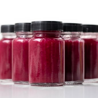 Shot glasses with black lids on filled with Superfood Blueberry Lemon Shot on a white table lined up.