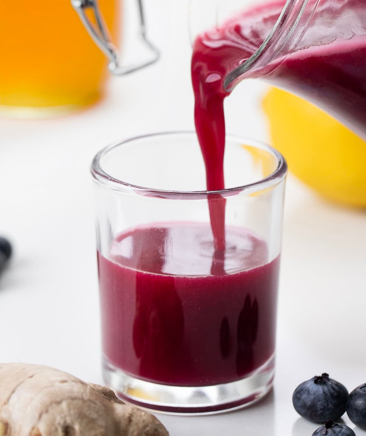Superfood Blueberry Lemon Shots are a quick, refreshing wellness drink packed with antioxidants. Made with fresh blueberries, zesty lemon, and a hint of ginger, these healthy shots are naturally sweetened with honey and blended with coconut water. Pouring Superfood Blueberry Lemon Shot into a shot glass.