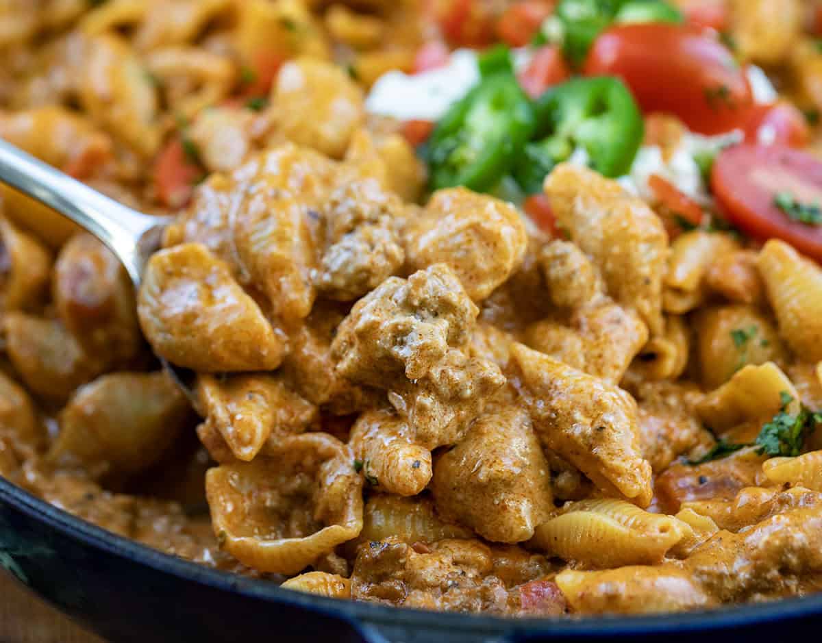 Get dinner on the table fast with this creamy, cheesy one-pot taco pasta! Packed with seasoned ground beef, tender shell pasta, and a rich, savory sauce, it’s a comforting taco-inspired meal the whole family will love on busy weeknights! Close up of a scoop of Taco Pasta being held above the pan.
