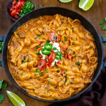 Pan of Taco Pasta on a wooden table with fresh tomatoes, jalapeno, and lime wedges.