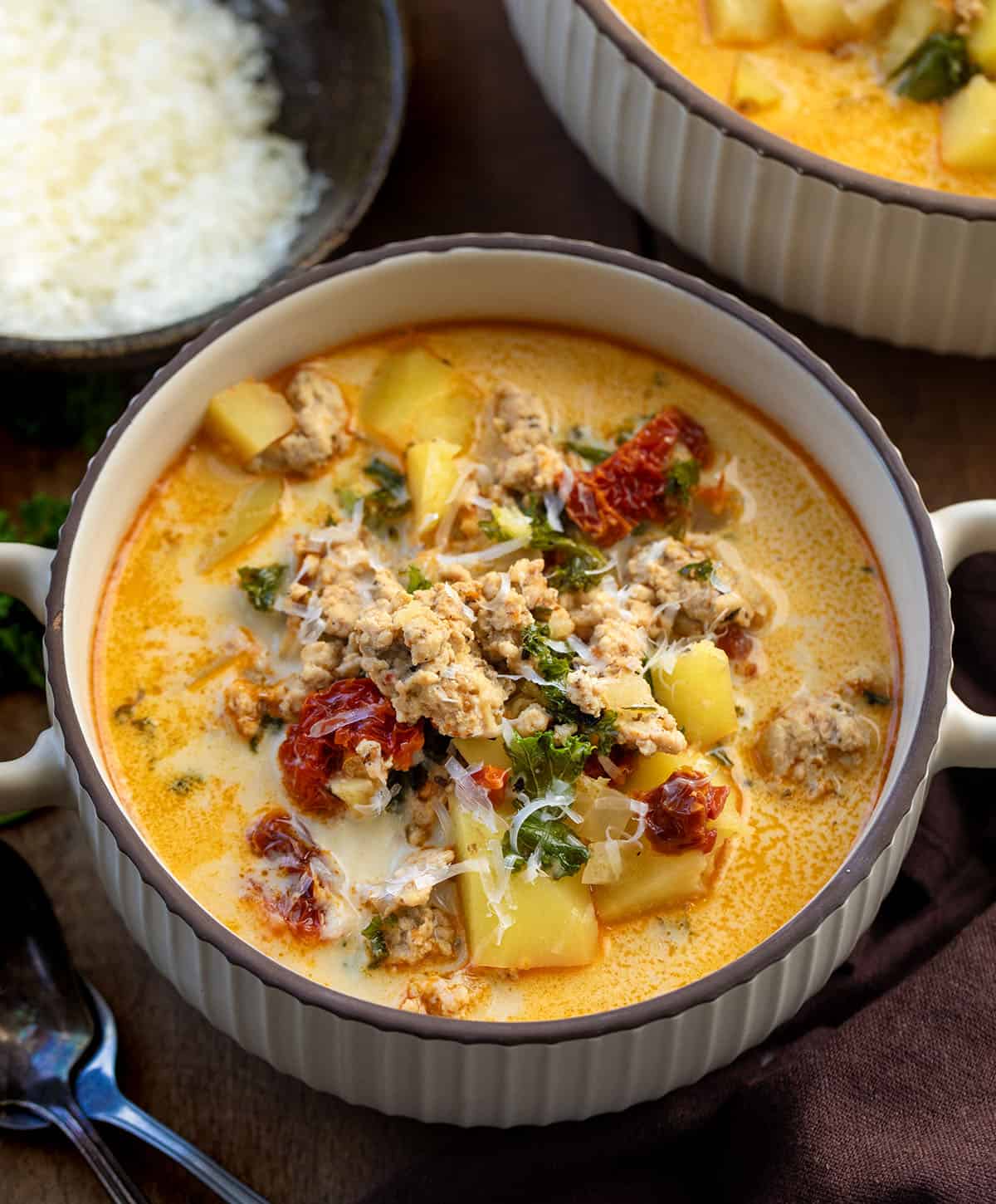 Warm, cozy, and packed with flavor, this Tuscan Chicken Potato Soup is a comforting one-pot meal you’ll want to make again and again! Bowls of Tuscan Chicken Potato Soup on a wooden table.
