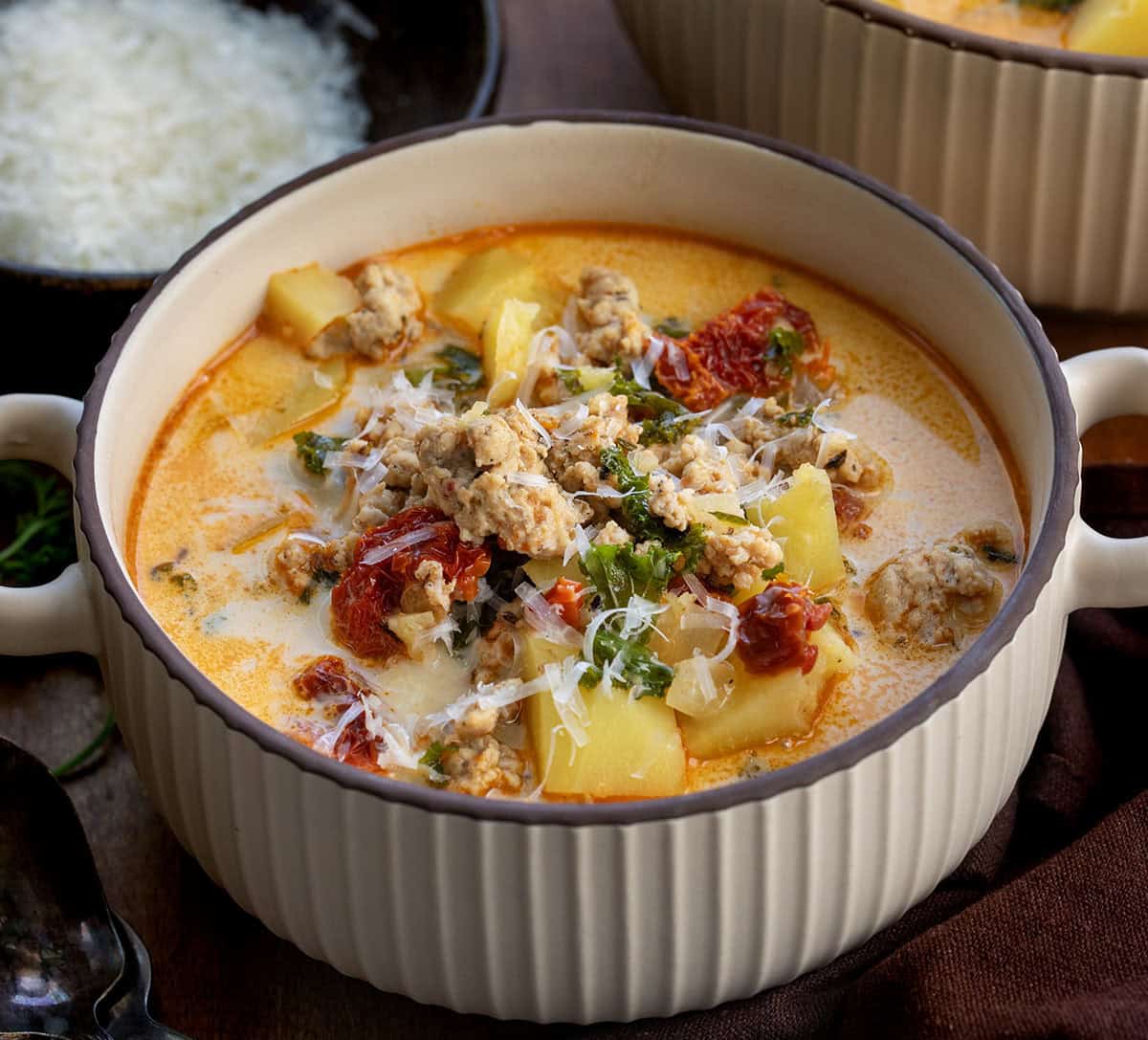 Warm, cozy, and packed with flavor, this Tuscan Chicken Potato Soup is a comforting one-pot meal you’ll want to make again and again! Bowls of Tuscan Chicken Potato Soup on a wooden table.