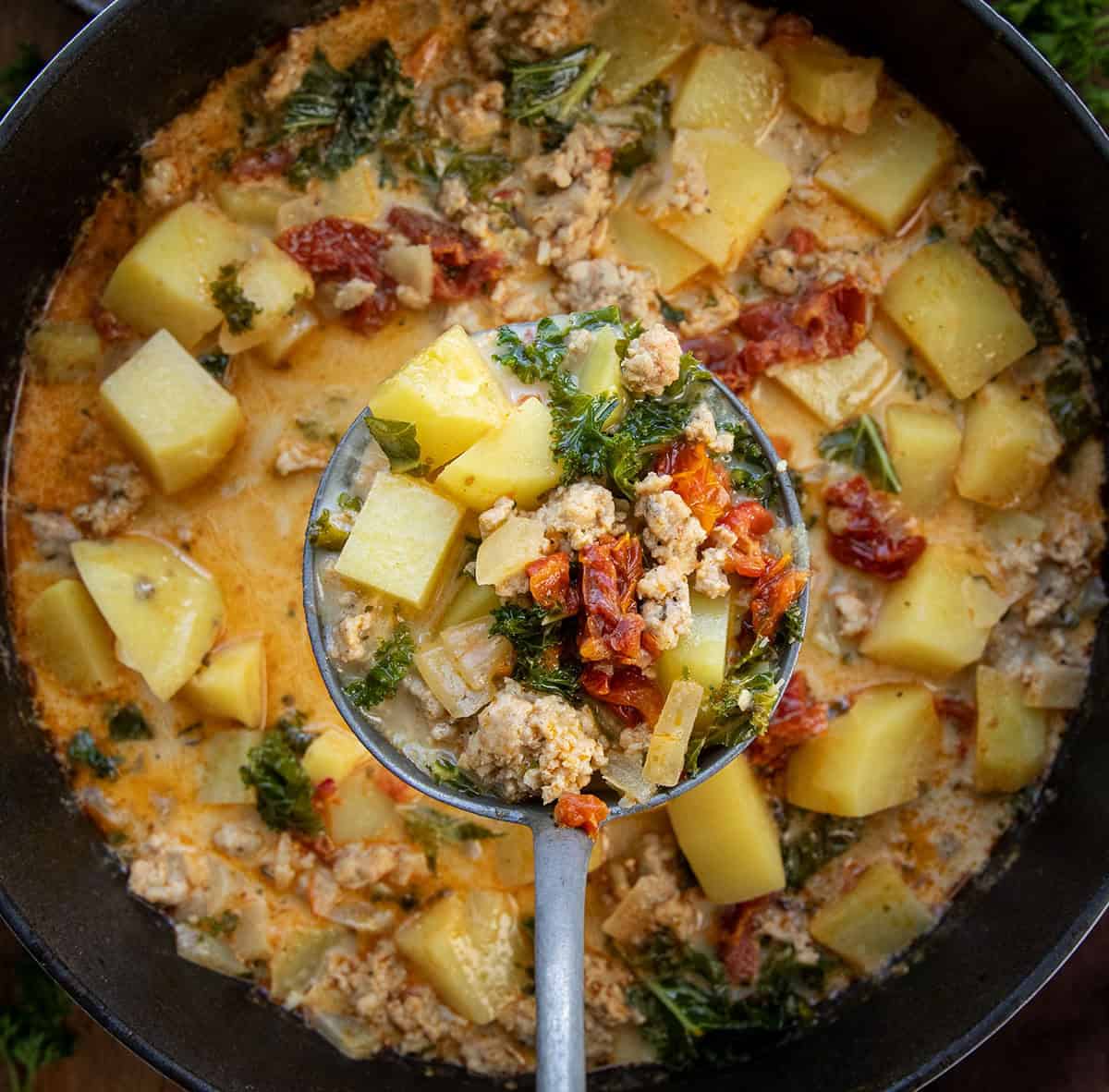 Warm, cozy, and packed with flavor, this Tuscan Chicken Potato Soup is a comforting one-pot meal you’ll want to make again and again! Ladle full of Tuscan Chicken Potato Soup being held above the pot.