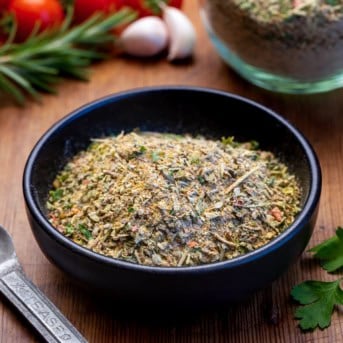 Small black container with Tuscan Seasoning in it on a wooden table.