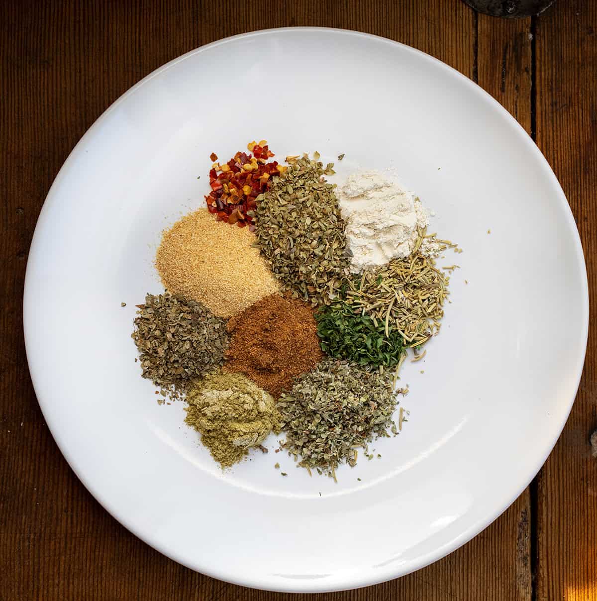 Homemade Tuscan Seasoning is a quick and easy spice blend that adds bold Italian flavor to your favorite meals. It’s made with dried herbs, garlic, and a touch of sun-dried tomato for a rich, savory taste! White plate with all the seasonings for Tuscan Seasoning.