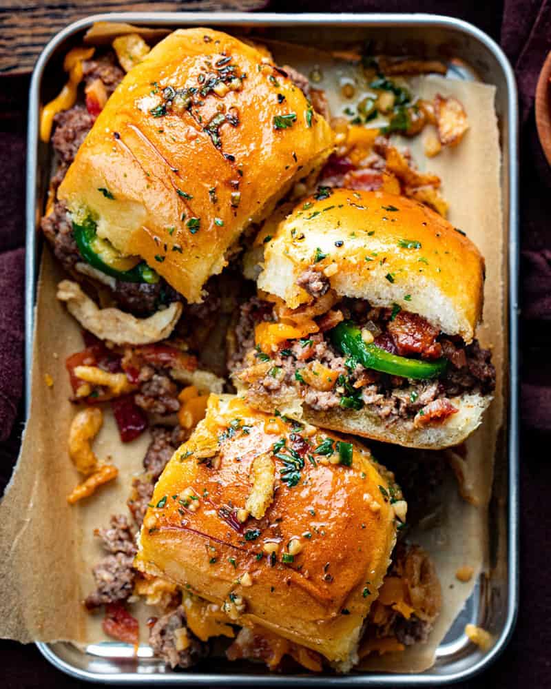 Sliders are one of the easiest ways to feed a crowd. They’re fun, customizable, and perfect for parties, game days, holidays, and family dinners! Platter with Cowboy Sliders in It Showing the Top and Sides and Ingredients Spilling out on a Cutting Board.