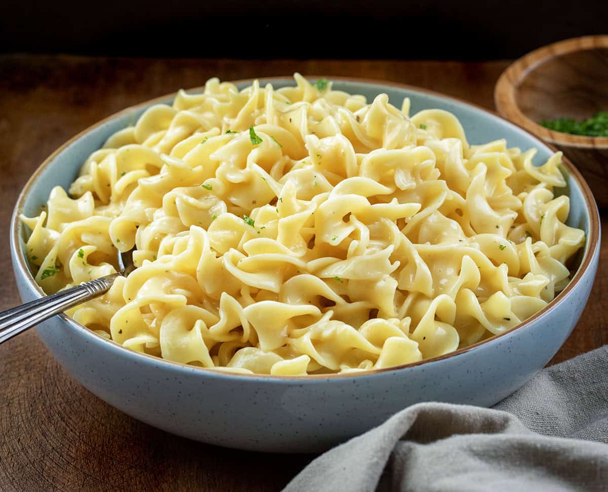 These Cafeteria Noodles are a simple, cozy one-pot recipe made with egg noodles simmered in chicken broth, then finished with cream of chicken soup, butter, and seasonings. They’re rich, creamy, and nostalgic, just like the comforting noodles you remember from school lunches. Blue bowl filled with Cafeteria Noodles on a wooden table.