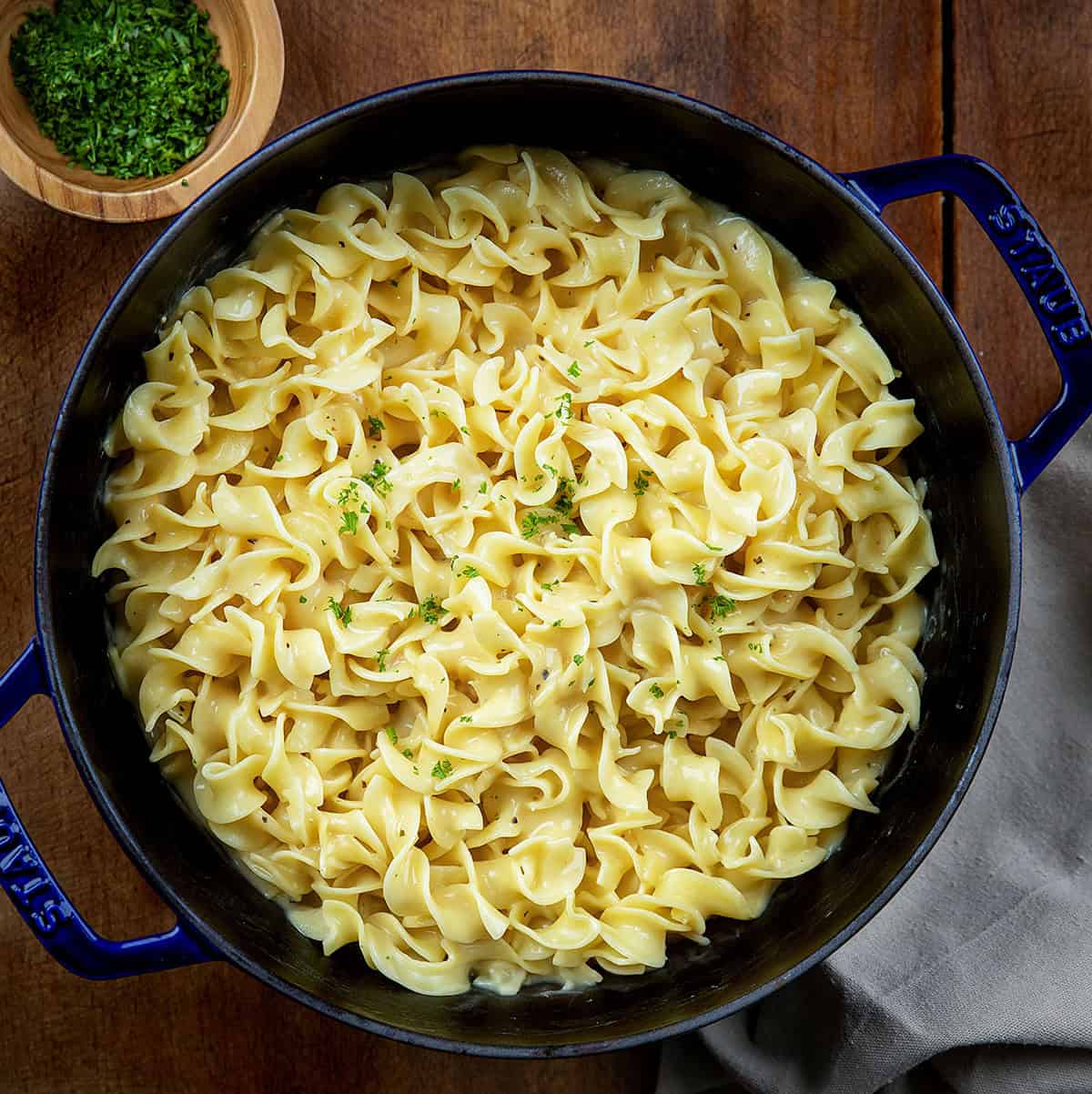These Cafeteria Noodles are a simple, cozy one-pot recipe made with egg noodles simmered in chicken broth, then finished with cream of chicken soup, butter, and seasonings. They’re rich, creamy, and nostalgic, just like the comforting noodles you remember from school lunches. Pot of Cafeteria Noodles on a wooden table from overhead.