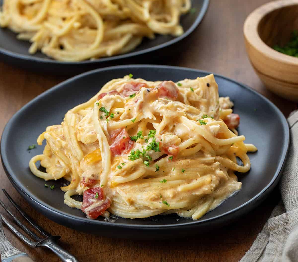 This Slow Cooker Cheesy Chicken Spaghetti is an easy, comforting dinner made with tender shredded chicken, a creamy cheese sauce, and perfectly cooked pasta! Black plates with creamy Slow Cooker Cheesy Chicken Spaghetti on them on a wooden table.