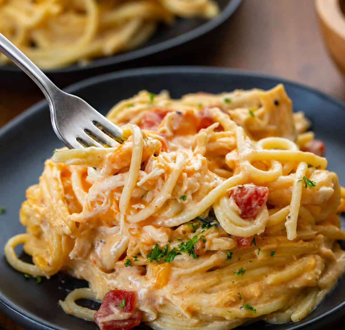This Slow Cooker Cheesy Chicken Spaghetti is an easy, comforting dinner made with tender shredded chicken, a creamy cheese sauce, and perfectly cooked pasta! Fork picking up a bite of Slow Cooker Cheesy Chicken Spaghetti from a black plate.