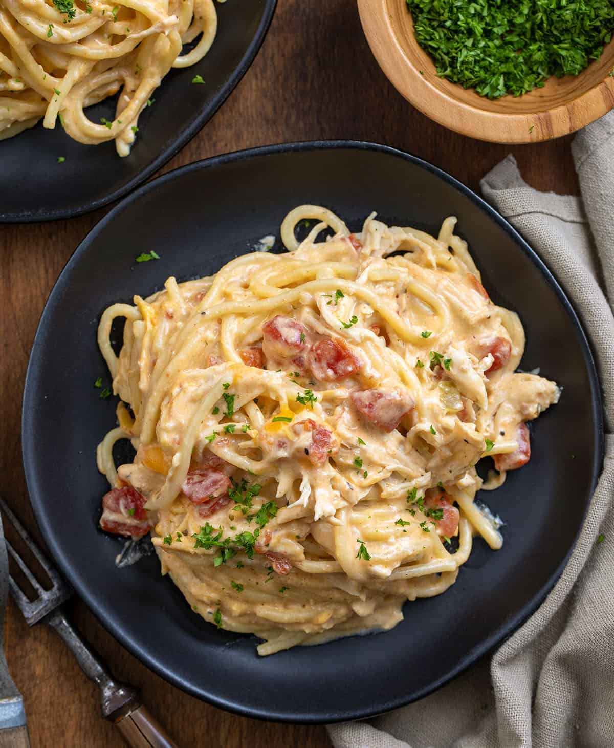 This Slow Cooker Cheesy Chicken Spaghetti is an easy, comforting dinner made with tender shredded chicken, a creamy cheese sauce, and perfectly cooked pasta! Black plates of Slow Cooker Cheesy Chicken Spaghetti on a wooden table from overhead.