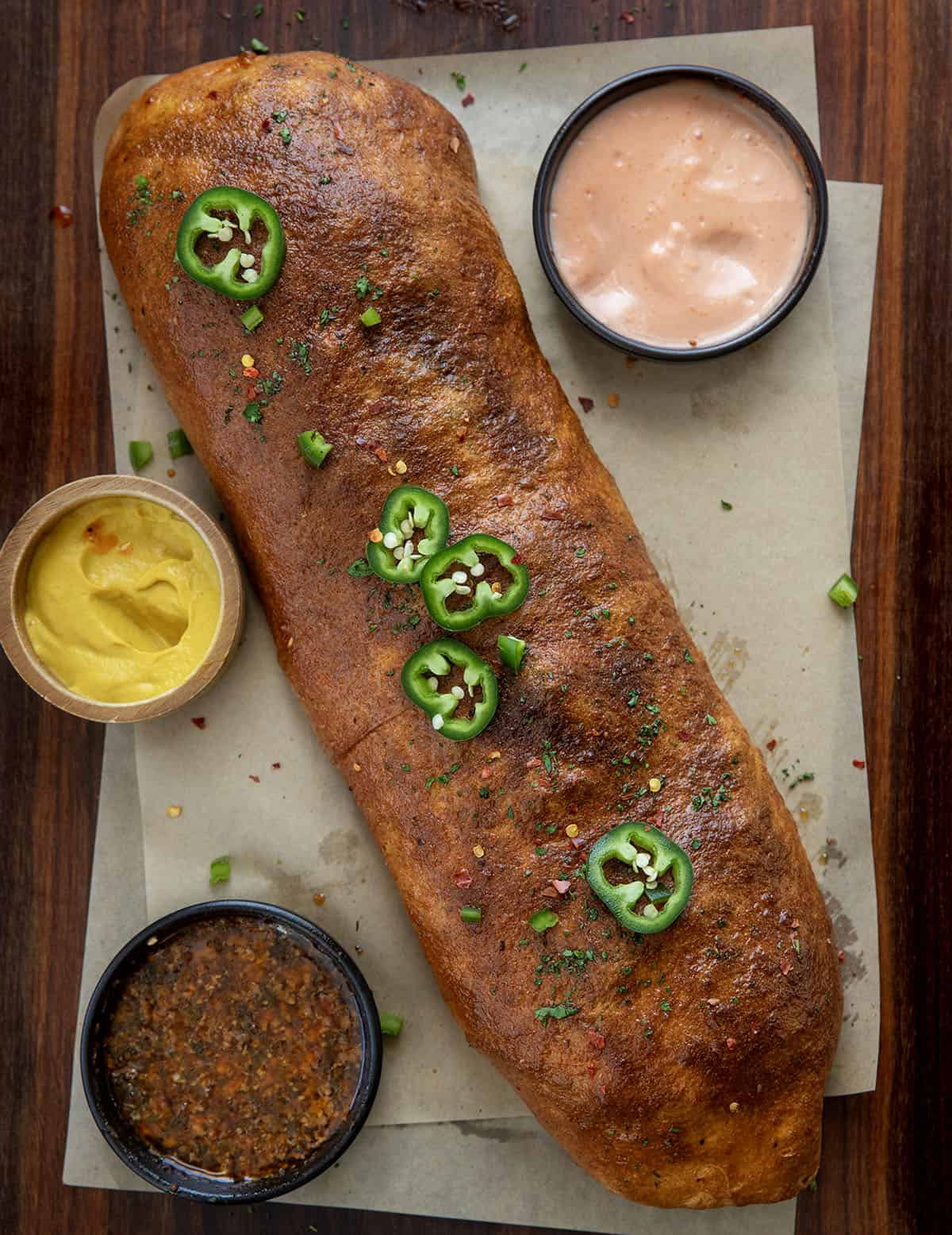 This Cowboy Garbage Bread is packed with seasoned ground beef, smoky bacon, sharp cheddar, and spicy jalapeños, all rolled up in golden pizza dough and brushed with flavorful Cowboy Butter! Whole Cowboy Garbage Bread on a wooden table from overhead.