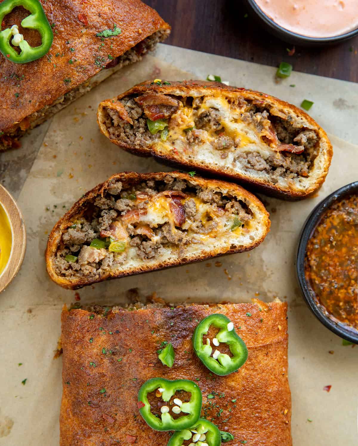 This Cowboy Garbage Bread is packed with seasoned ground beef, smoky bacon, sharp cheddar, and spicy jalapeños, all rolled up in golden pizza dough and brushed with flavorful Cowboy Butter! Cut pieces of Cowboy Garbage Bread laying flat next to the bread on a wooden table with cowboy butter.