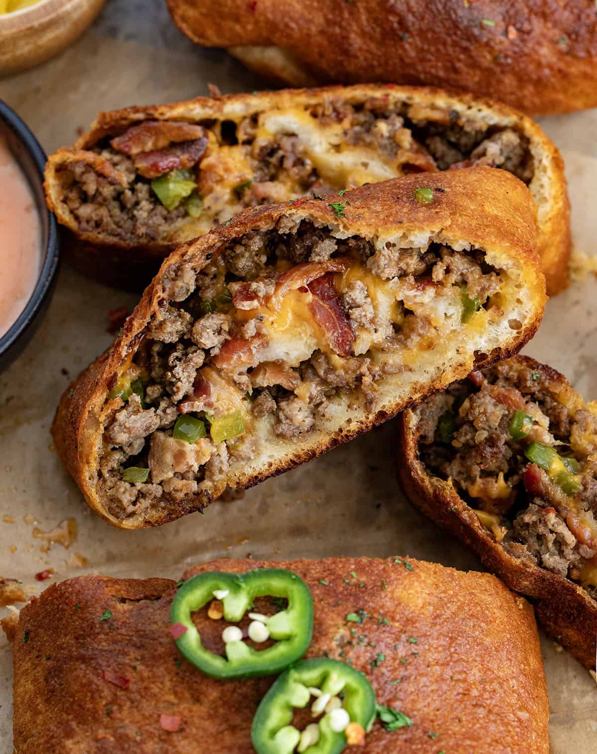 This Cowboy Garbage Bread is packed with seasoned ground beef, smoky bacon, sharp cheddar, and spicy jalapeños, all rolled up in golden pizza dough and brushed with flavorful Cowboy Butter! Cut into Cowboy Garbage Bread on a wooden table with fry sauce.
