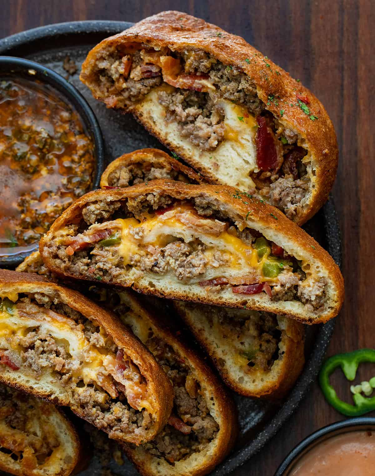 This Cowboy Garbage Bread is packed with seasoned ground beef, smoky bacon, sharp cheddar, and spicy jalapeños, all rolled up in golden pizza dough and brushed with flavorful Cowboy Butter! Slices of Cowboy Garbage Bread cut and on a platter with Cowboy Butter.