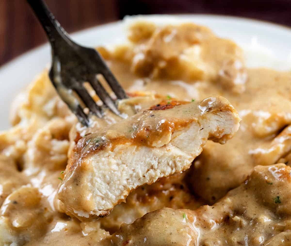 Easy Chicken and Gravy is a cozy, comforting dinner made with tender pan-seared chicken and a rich homemade onion gravy. Fork holding a piece of Easy Chicken and Gravy.