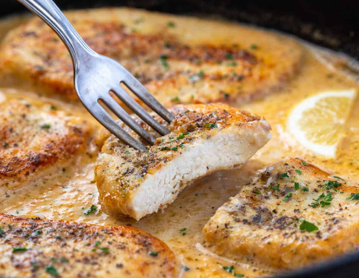 These Creamy Garlic Chicken Breasts are juicy, tender, and smothered in a rich, cheesy garlic sauce. Perfect over rice, pasta, or mashed potatoes for an easy weeknight or special dinner! Fork holding a piece of Garlic Chicken Breast.