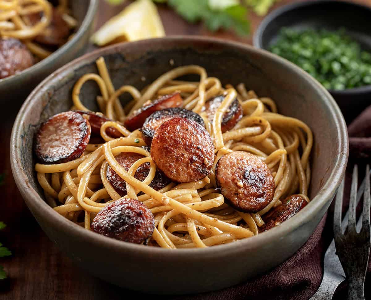 Creamy, garlicky linguine with smoky kielbasa and a touch of heat from sriracha. Quick, flavorful, and perfect for an easy weeknight dinner. Brown bowl filled with Garlic Pasta with Kielbasa on a wooden table.