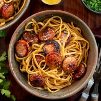 Bowls of Garlic Pasta with Kielbasa on a wooden table from overhead.