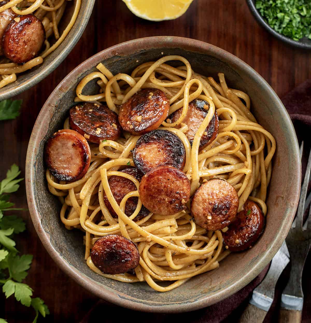 Creamy, garlicky linguine with smoky kielbasa and a touch of heat from sriracha. Quick, flavorful, and perfect for an easy weeknight dinner. Bowls of Garlic Pasta with Kielbasa on a wooden table from overhead.