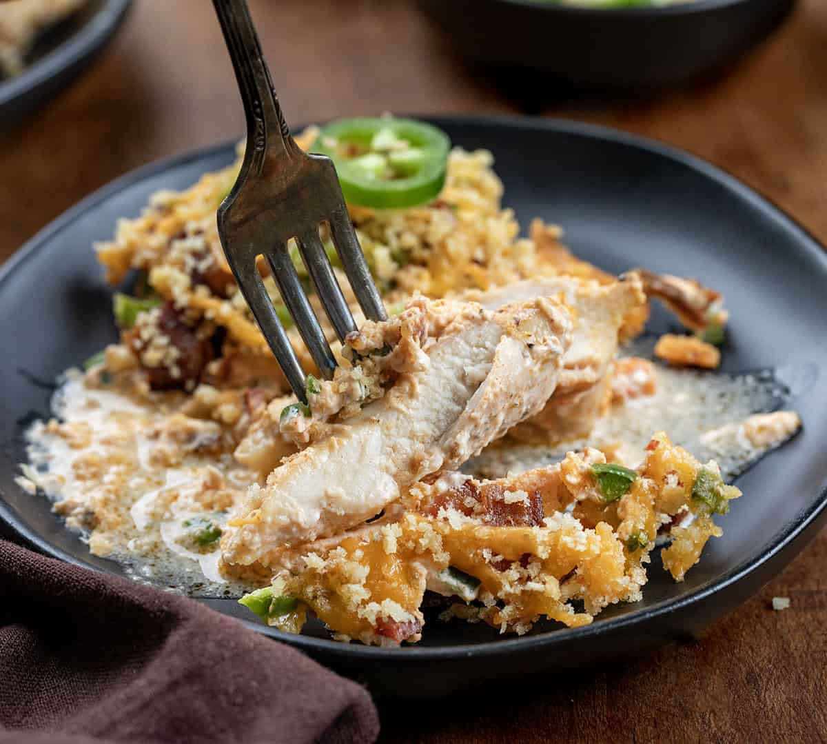 This Jalapeño Popper Chicken Bake is creamy, cheesy, and full of bold flavor in every bite. Tender chicken thighs are baked in a rich cream cheese sauce, then topped with crispy bacon, fresh jalapeños, and melty cheddar, all finished with a golden panko topping! Fork picking up a piece of cut Jalapeño Popper Chicken.