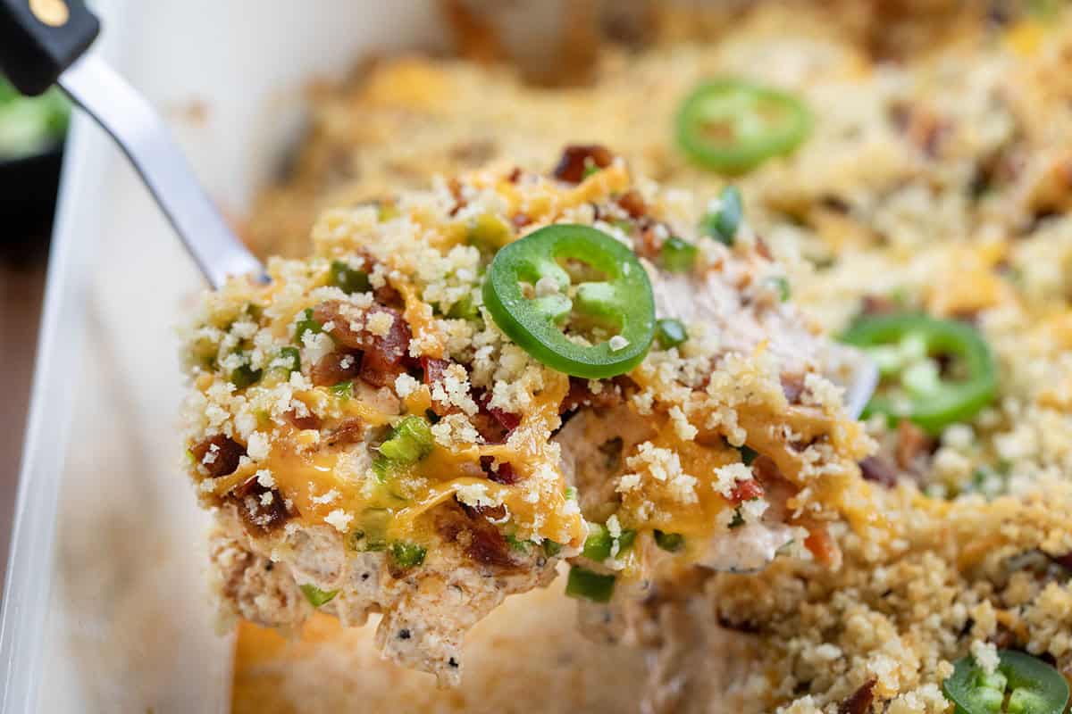 This Jalapeño Popper Chicken Bake is creamy, cheesy, and full of bold flavor in every bite. Tender chicken thighs are baked in a rich cream cheese sauce, then topped with crispy bacon, fresh jalapeños, and melty cheddar, all finished with a golden panko topping! Spatula picking up a piece of Jalapeño Popper Chicken from the pan.