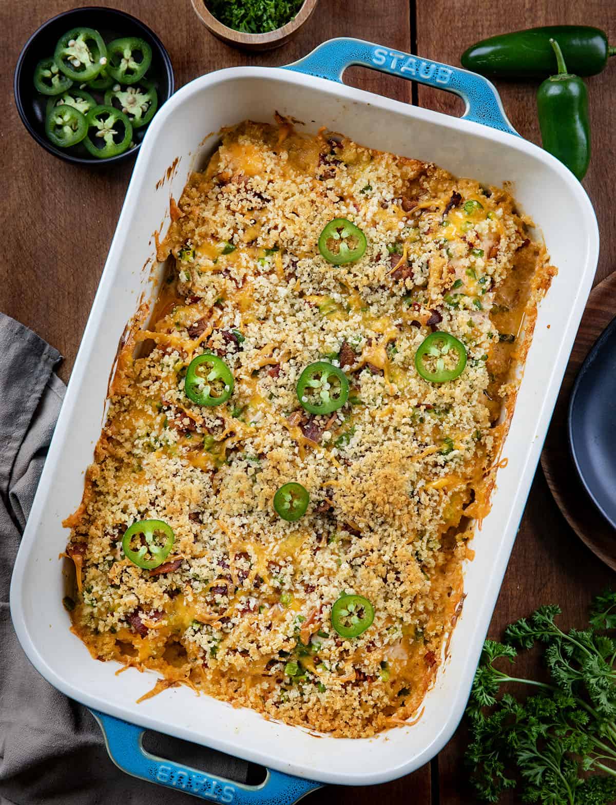 This Jalapeño Popper Chicken Bake is creamy, cheesy, and full of bold flavor in every bite. Tender chicken thighs are baked in a rich cream cheese sauce, then topped with crispy bacon, fresh jalapeños, and melty cheddar, all finished with a golden panko topping! Pan of Jalapeño Popper Chicken on a wooden table from overhead.