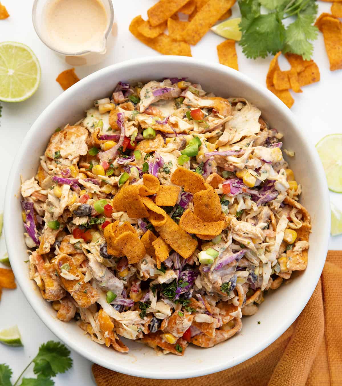 This Loaded Chicken Frito Cowboy Cabbage is a hearty, flavor-packed salad made with crunchy cabbage, shredded rotisserie chicken, black beans, corn, and fresh veggies, all tossed in a creamy chipotle dressing and finished with Chili Cheese Fritos! White bowl filled with Loaded Chicken Frito Cowboy Cabbage on a white table with fresh lime and cilantro.