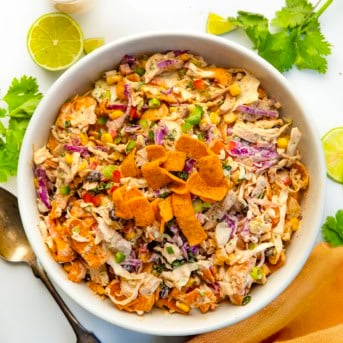 White bowl filled with Loaded Chicken Frito Cowboy Cabbage on a white table with fresh lime and cilantro.