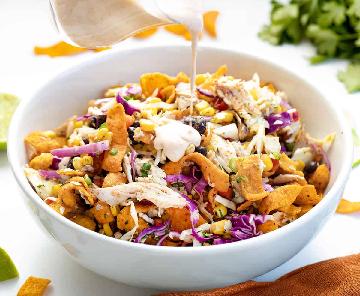 This Loaded Chicken Frito Cowboy Cabbage is a hearty, flavor-packed salad made with crunchy cabbage, shredded rotisserie chicken, black beans, corn, and fresh veggies, all tossed in a creamy chipotle dressing and finished with Chili Cheese Fritos! Pouring Chipotle Lime Dressing over Loaded Chicken Frito Cowboy Cabbage.