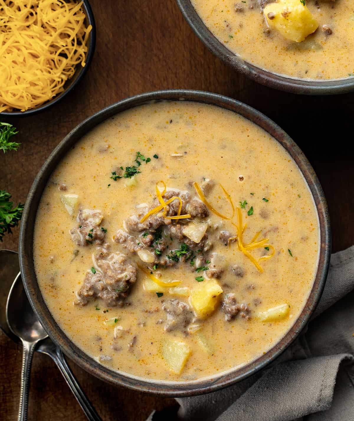 Ranch Cheesy Beef and Potato Soup is a rich and creamy soup made with ground beef, tender potatoes, cheddar cheese, and ranch seasoning! Bowls of Ranch Cheesy Beef and Potato Soup on a wooden table from overhead.