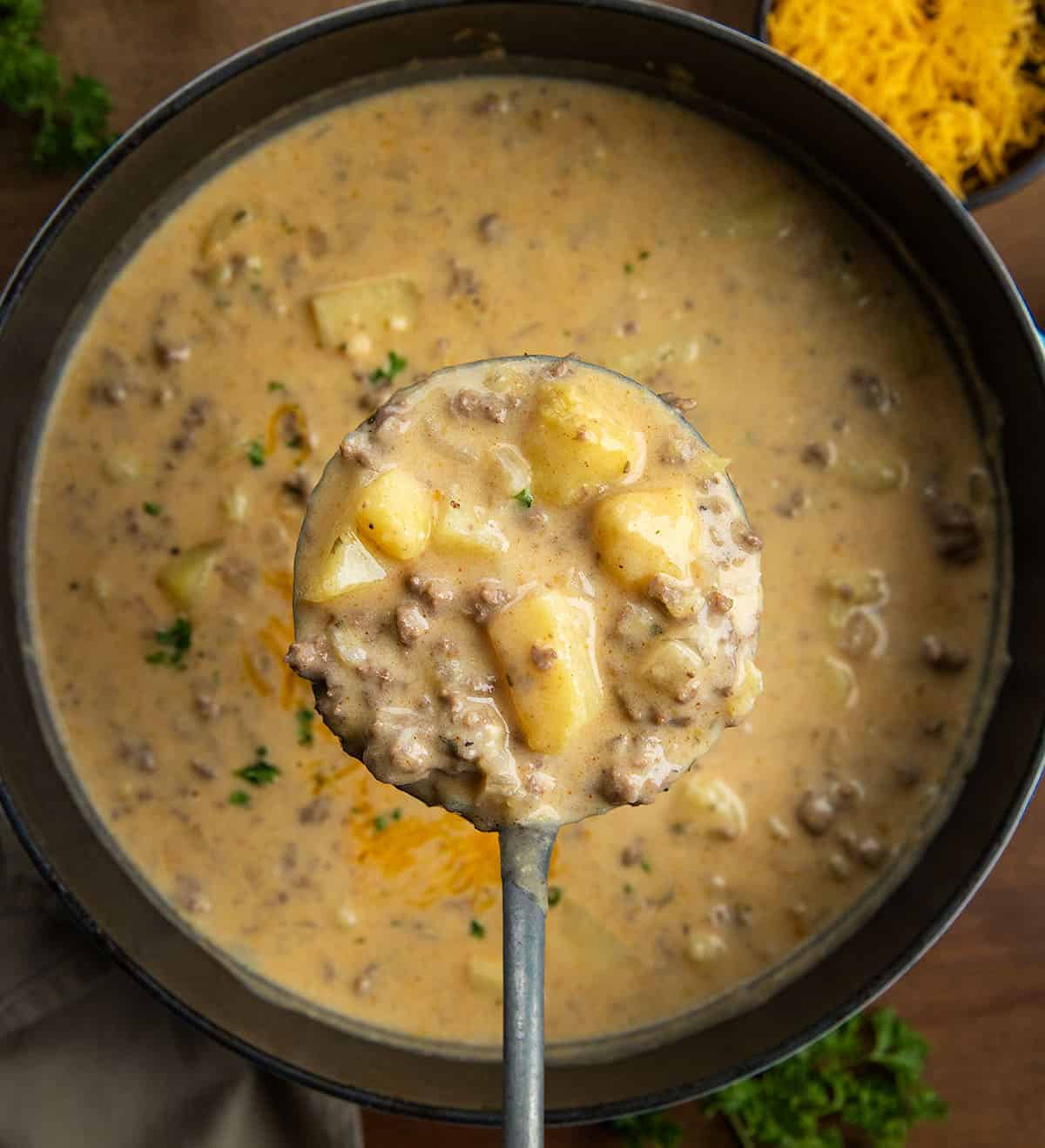 Ranch Cheesy Beef and Potato Soup is a rich and creamy soup made with ground beef, tender potatoes, cheddar cheese, and ranch seasoning! Ladle full of Ranch Cheesy Beef and Potato Soup being held above the pot from overhead.