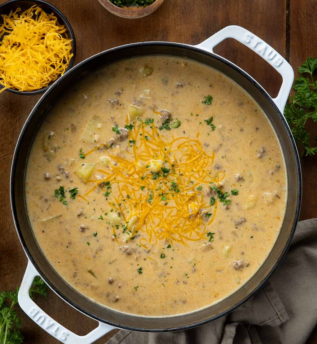Ranch Cheesy Beef and Potato Soup is a rich and creamy soup made with ground beef, tender potatoes, cheddar cheese, and ranch seasoning! White pot of Ranch Cheesy Beef and Potato Soup on a wooden table from overhead.