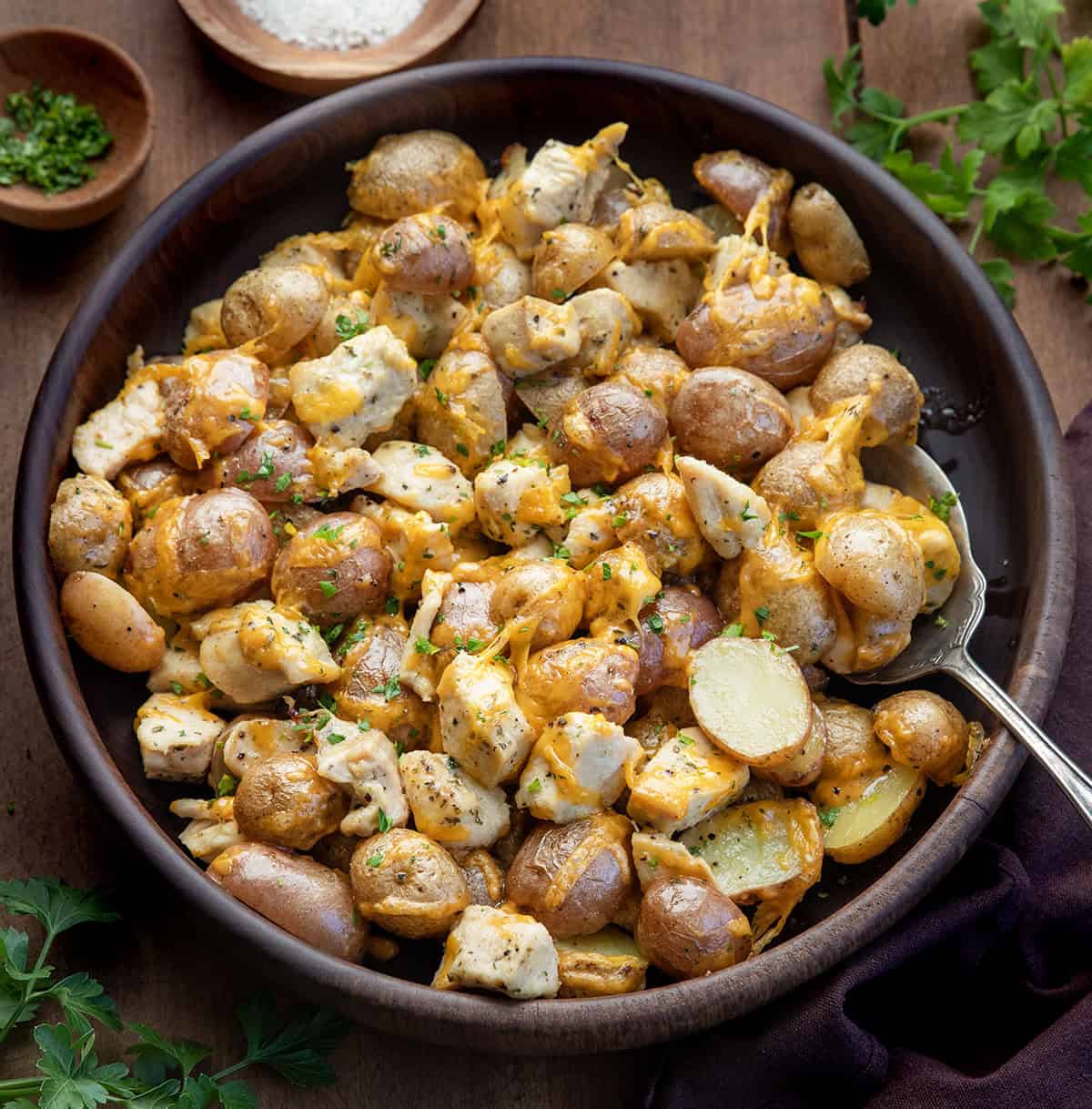This One Pan Ranch Chicken and Potatoes is an easy sheet pan dinner made with tender chicken, roasted potatoes, and bold ranch seasoning, all finished with melted cheddar cheese! Wooden serving bowl filled with One Pan Ranch Chicken and Potatoes with a spoon in the bowl.