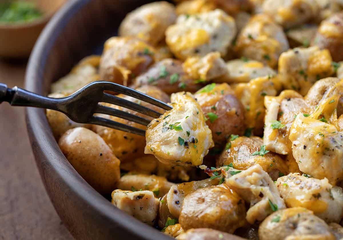 This One Pan Ranch Chicken and Potatoes is an easy sheet pan dinner made with tender chicken, roasted potatoes, and bold ranch seasoning, all finished with melted cheddar cheese! Close up of a fork picking up a piece of Ranch Chicken.