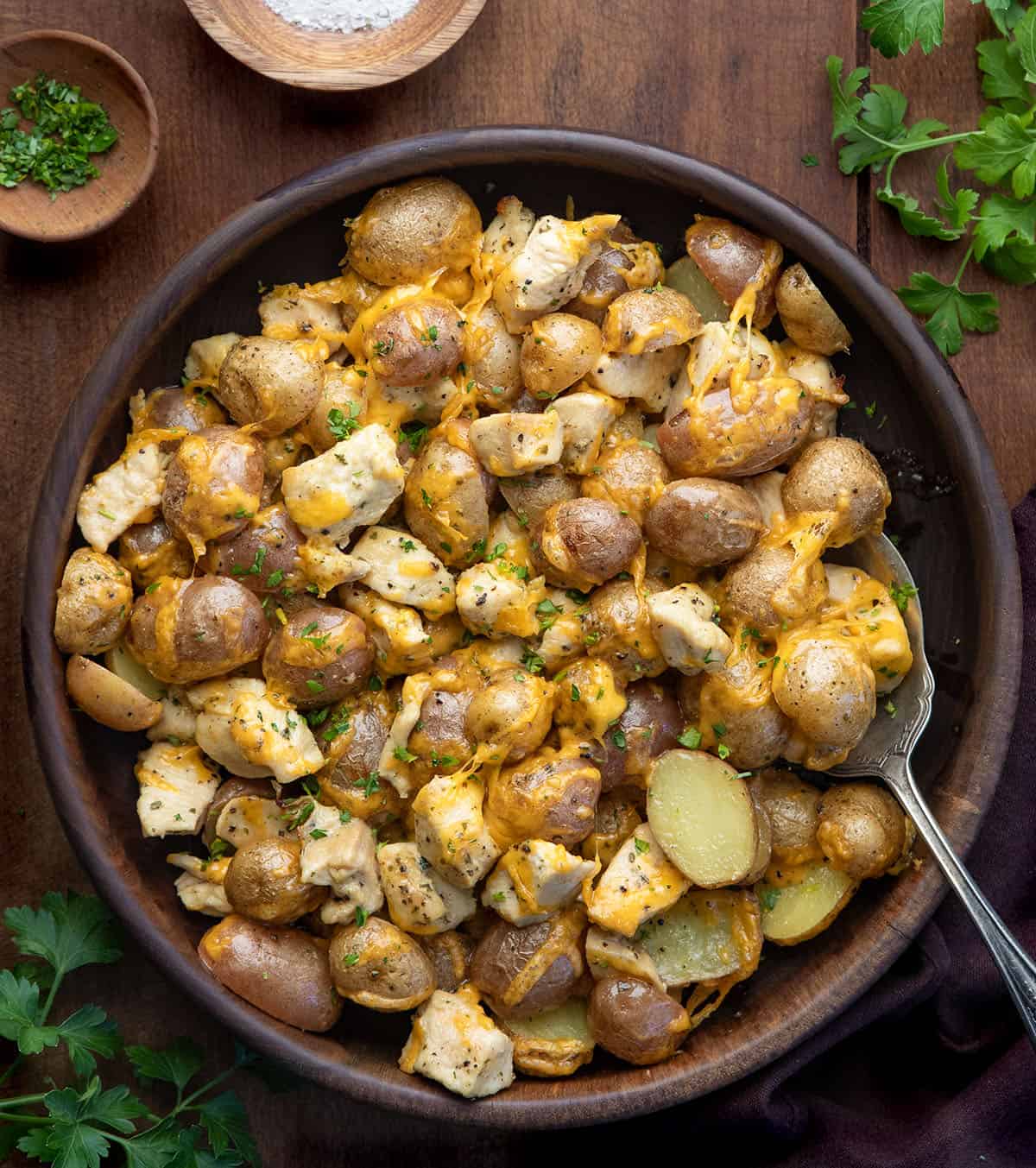 This One Pan Ranch Chicken and Potatoes is an easy sheet pan dinner made with tender chicken, roasted potatoes, and bold ranch seasoning, all finished with melted cheddar cheese! Wooden serving bowl filled with Ranch Chicken and Potatoes on a wooden table from overhead.