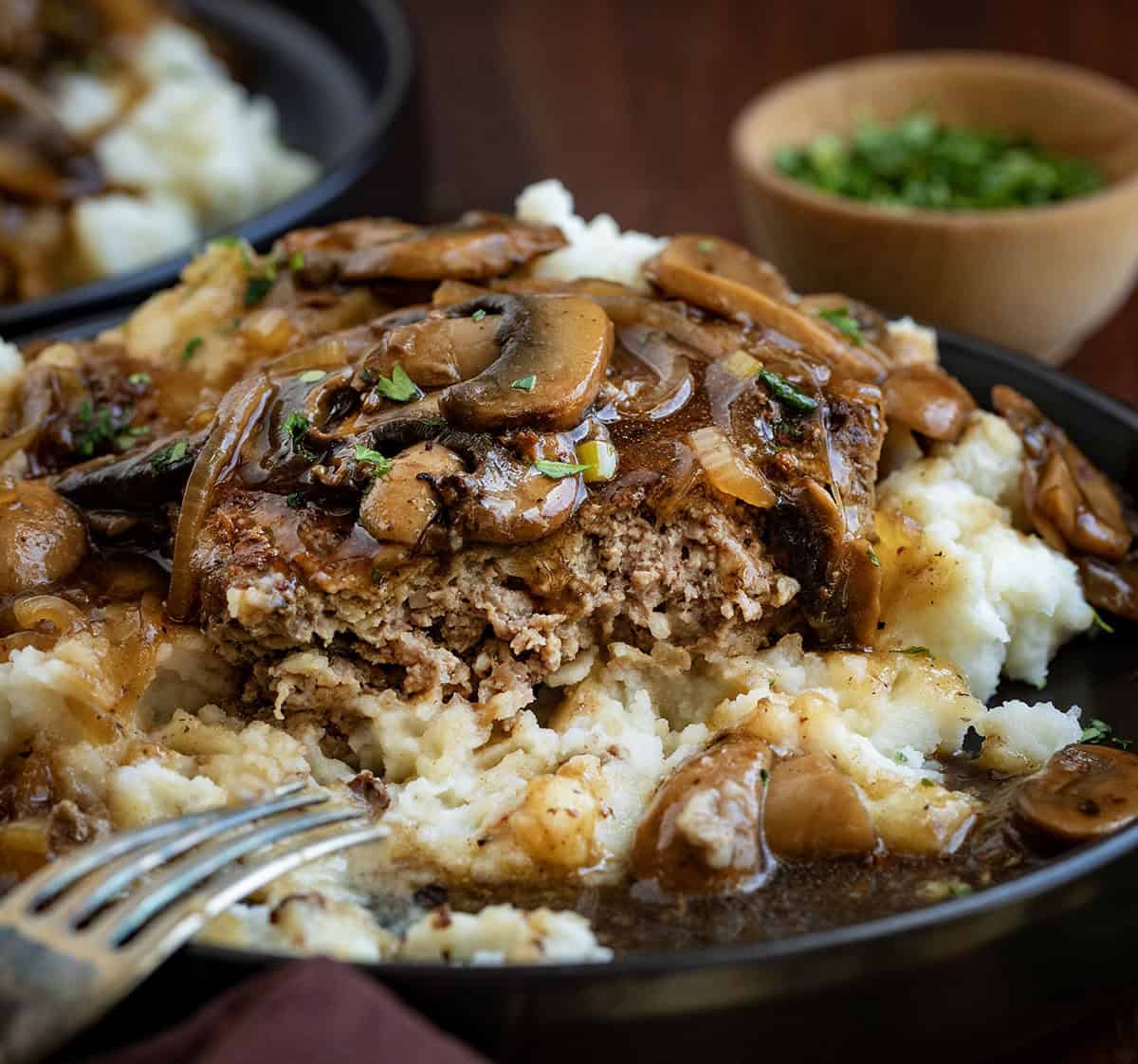 Poor Man’s Salisbury Steak with Mushrooms is an easy, budget-friendly dinner made with tender beef patties and a rich onion-mushroom gravy. It has all the classic comfort food flavor, with mushrooms adding even more depth to the savory sauce! One piece of Salisbury Steak with Mushrooms on a bed of mashed potatoes on a black plate.
