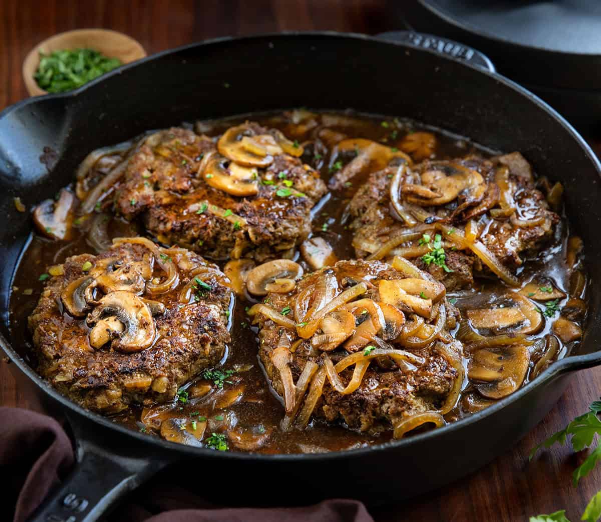Poor Man’s Salisbury Steak with Mushrooms is an easy, budget-friendly dinner made with tender beef patties and a rich onion-mushroom gravy. It has all the classic comfort food flavor, with mushrooms adding even more depth to the savory sauce! Salisbury Steak with Mushrooms in a black skillet on a wooden table.