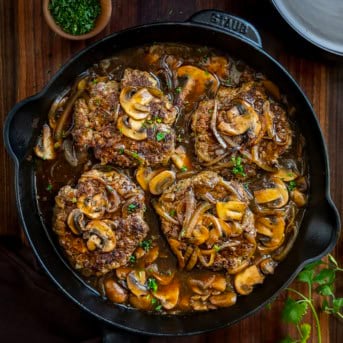 Black skillet of Salisbury Steak with Mushrooms on a wooden table from overhead.