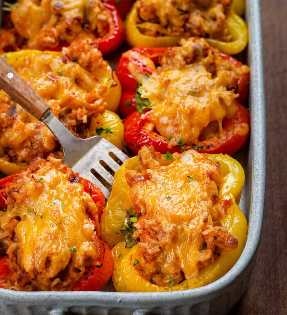 These Seafood Stuffed Bell Peppers are colorful, flavorful, and surprisingly easy to make. Sweet bell peppers cradle a tender mix of shrimp, jumbo lump crab, and seasoned rice, all topped with melted cheddar cheese! Spatula picking up a Seafood Stuffed Bell Pepper.