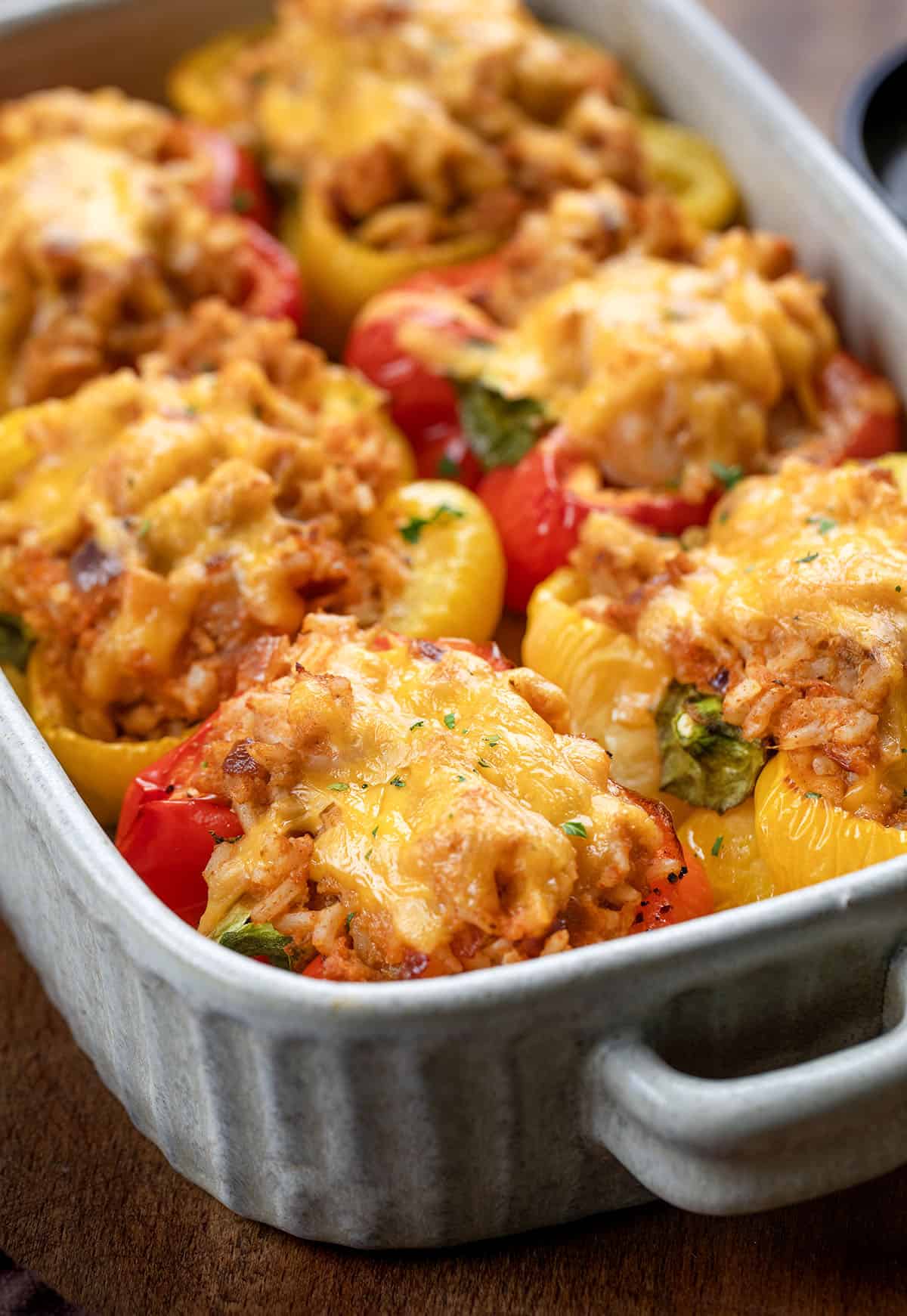 These Seafood Stuffed Bell Peppers are colorful, flavorful, and surprisingly easy to make. Sweet bell peppers cradle a tender mix of shrimp, jumbo lump crab, and seasoned rice, all topped with melted cheddar cheese! Close up of Seafood Stuffed Bell Peppers in a pan.