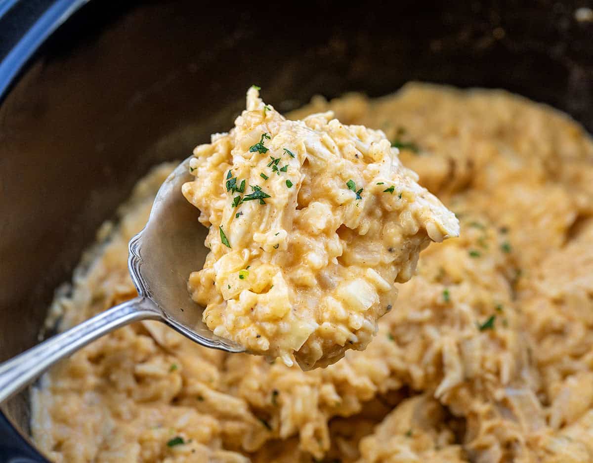 This Slow Cooker Chicken and Rice is a warm, comforting meal with tender chicken and creamy, flavorful rice cooked right in the crockpot! Spoonful of Slow Cooker Chicken and Rice being held above the slow cooker.