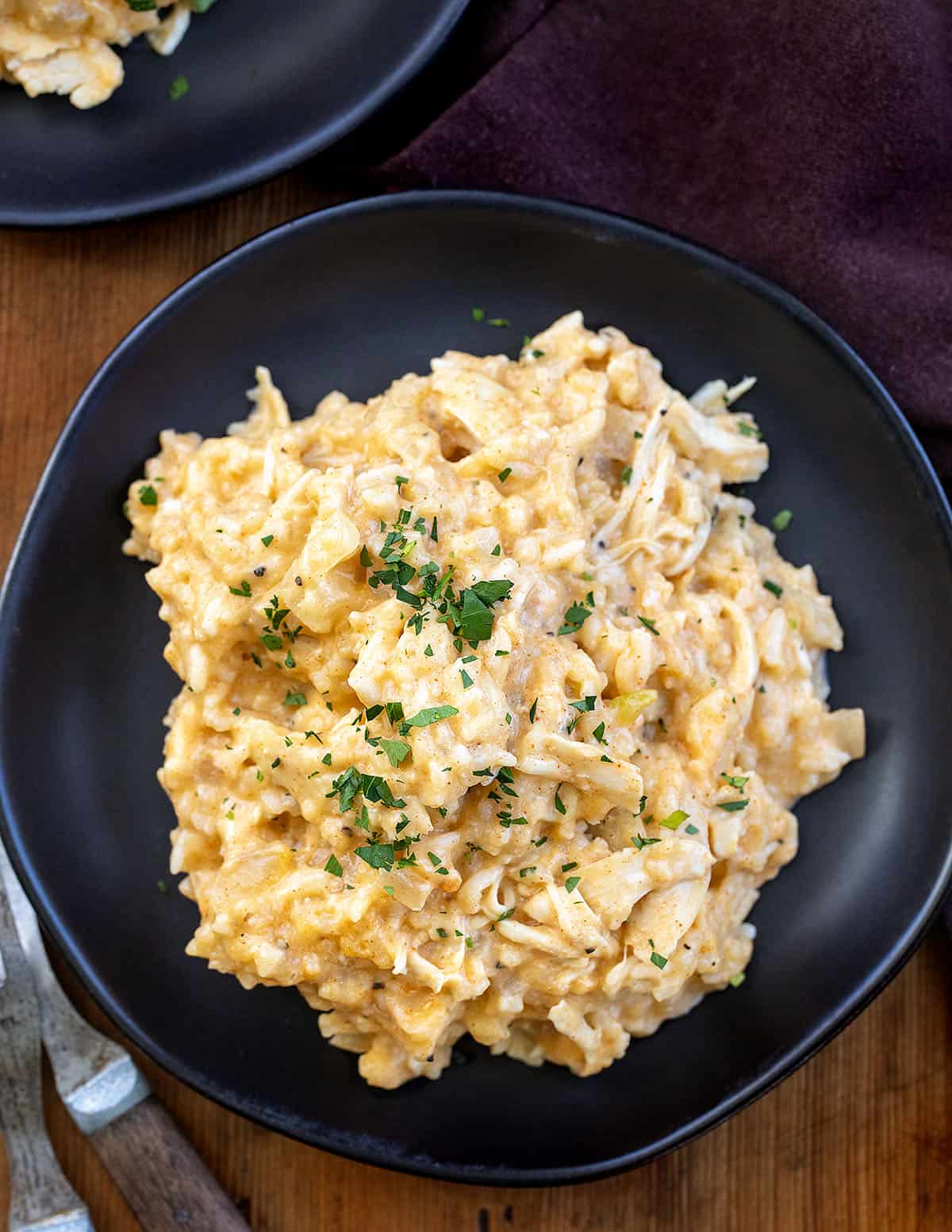 This Slow Cooker Chicken and Rice is a warm, comforting meal with tender chicken and creamy, flavorful rice cooked right in the crockpot! Black plates with Slow Cooker Chicken and Rice on them on a wooden table from overhead.