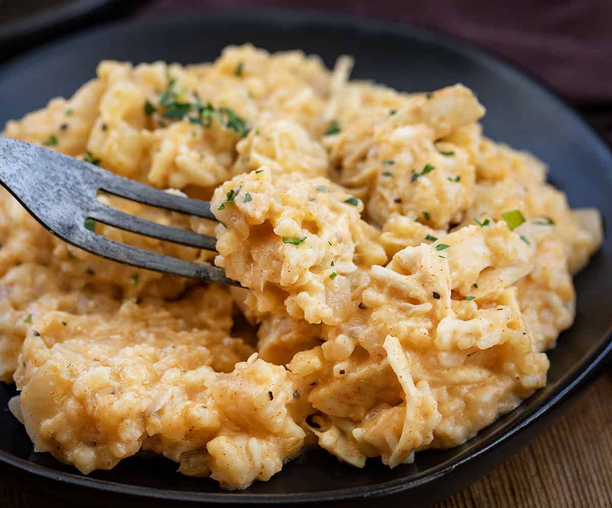 This Slow Cooker Chicken and Rice is a warm, comforting meal with tender chicken and creamy, flavorful rice cooked right in the crockpot! Fork picking up a bite of Slow Cooker Chicken and Rice from a black plate.