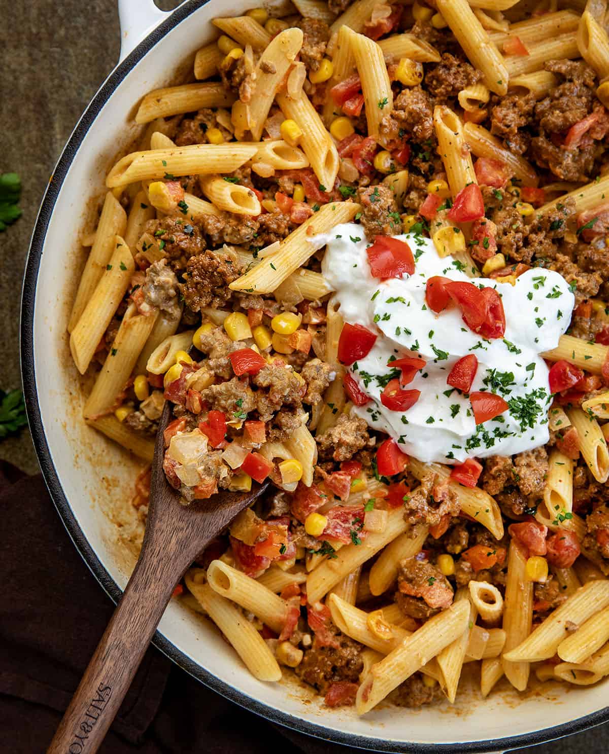 This Southwest Ground Beef Pasta is creamy, cheesy, and full of bold Southwest flavors. Easy to make, flexible with ingredients, and perfect for meal prep! Wooden spoon in a skillet with Southwest Ground Beef Pasta.