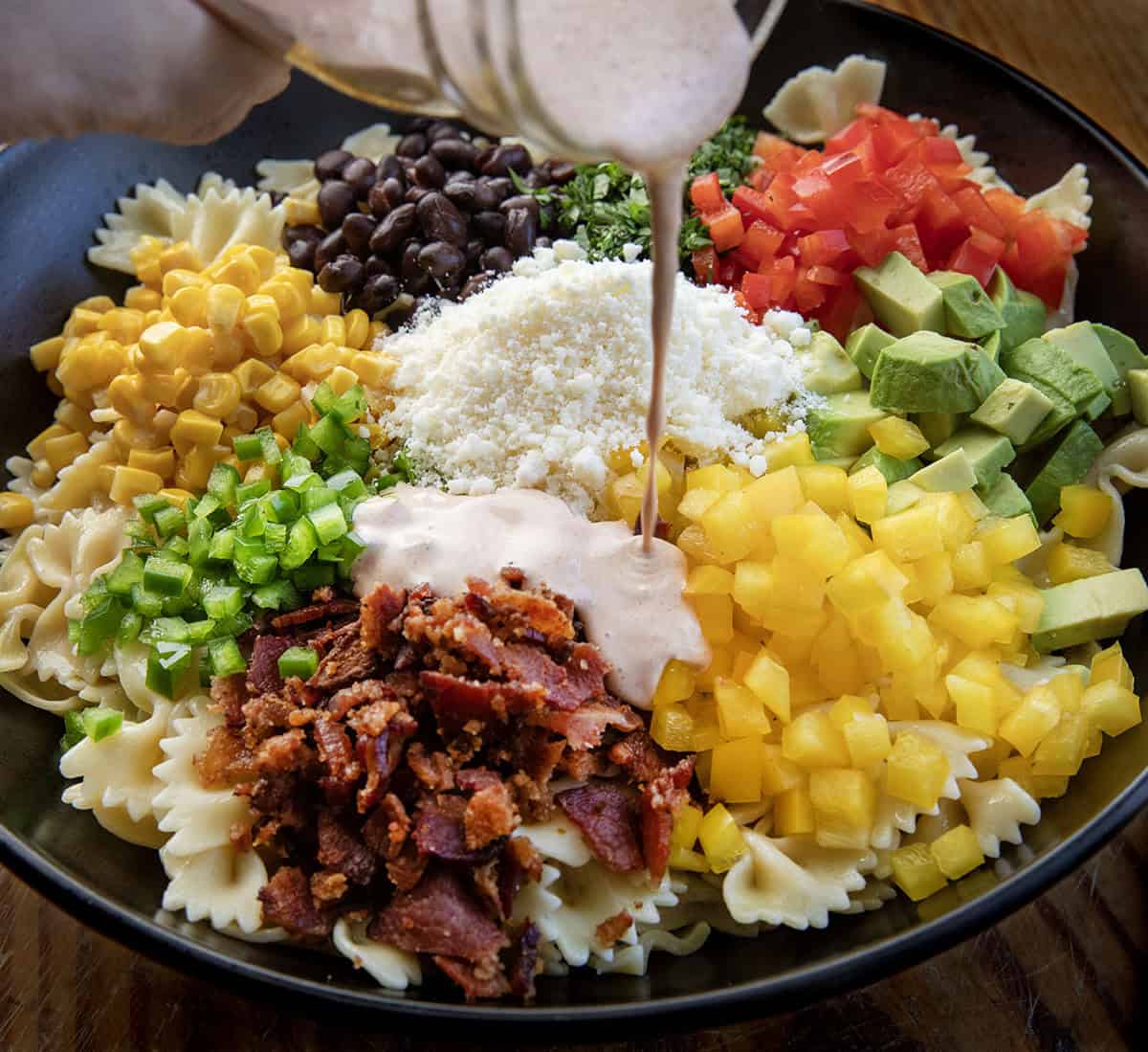 This Southwest Pasta Salad is bold, creamy, and packed with flavor in every bite. Made with bowtie pasta, black beans, corn, bacon, fresh veggies, and a chili-lime dressing, it’s an easy make-ahead dish that’s fresh, hearty, and full of Southwest flavor! Drizzling dressing over Southwest Pasta Salad before it is mixed in.