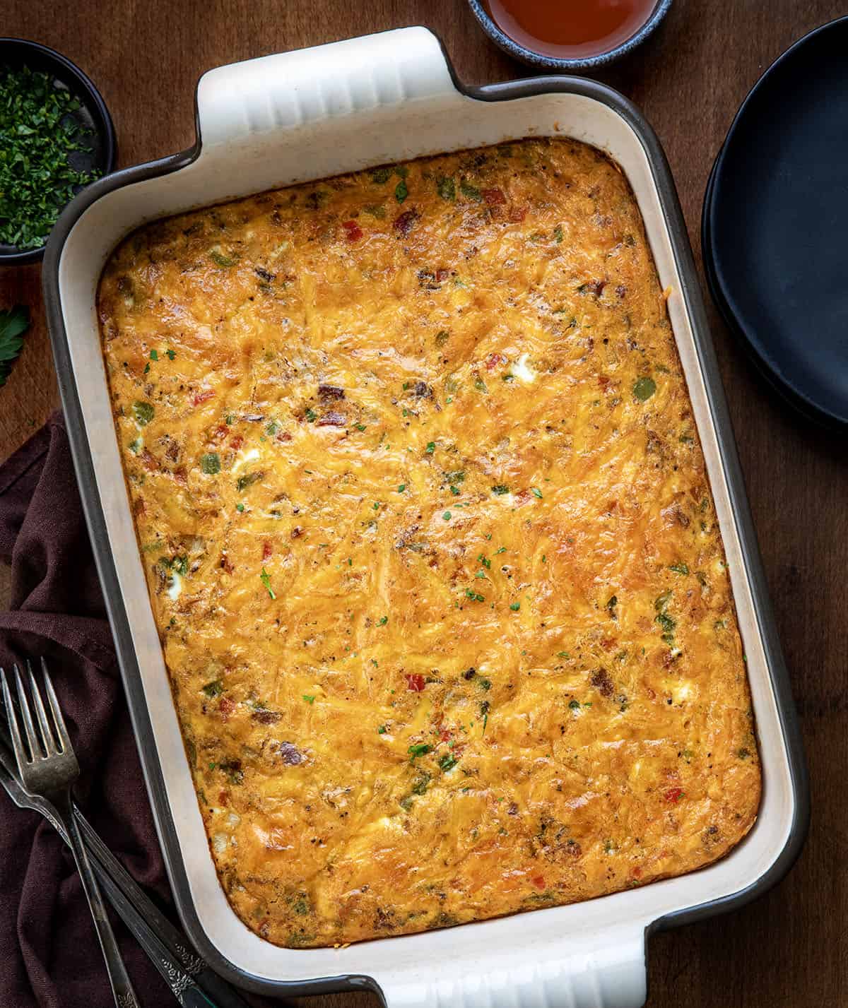 This Western Omelette Breakfast Bake is a quick, family-friendly breakfast that combines fluffy eggs, smoky bacon, sautéed peppers and onions, and melty cheddar cheese, all baked in one dish! Pan of Western Omelette Breakfast Bake on a wooden table from overhead.