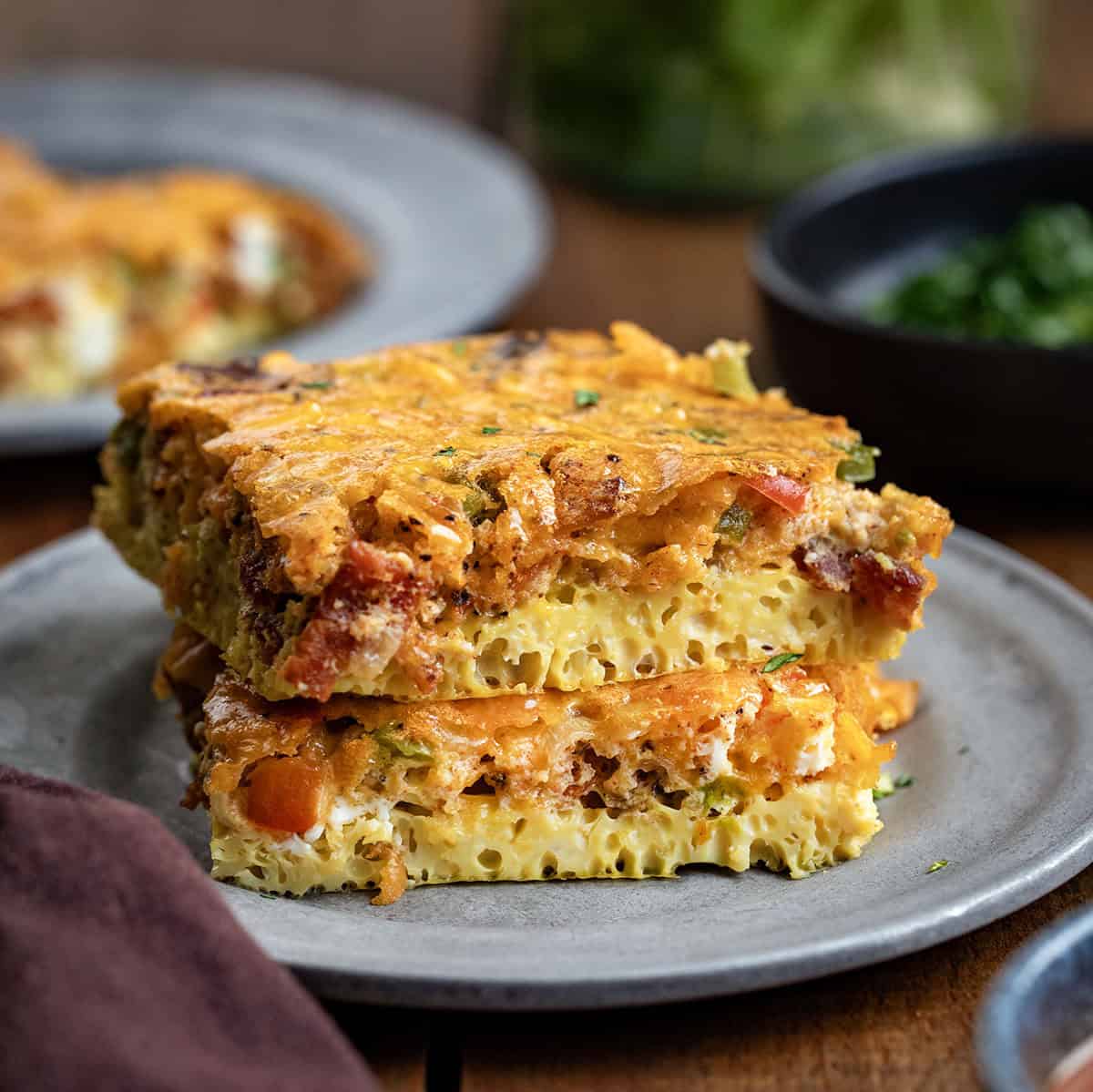 This Western Omelette Breakfast Bake is a quick, family-friendly breakfast that combines fluffy eggs, smoky bacon, sautéed peppers and onions, and melty cheddar cheese, all baked in one dish! Pieces of Western Omelette Breakfast Bakeon a plate close up.