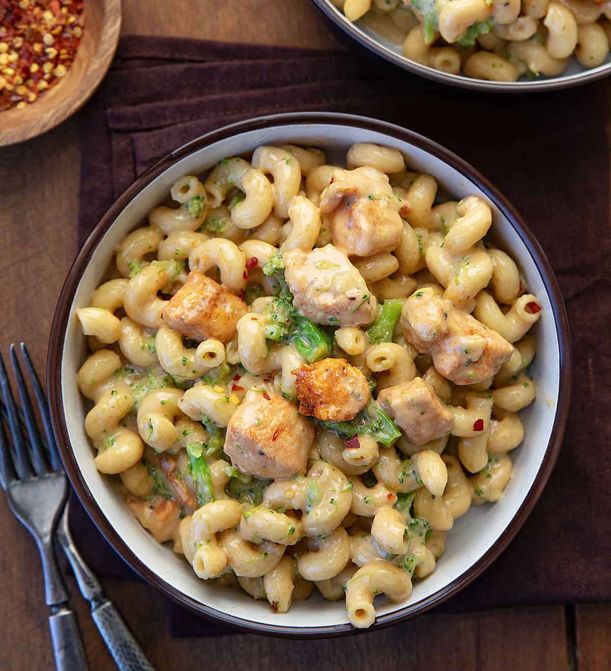 This White Cheddar Chicken Pasta with Broccoli is a creamy, comforting dinner made with tender chicken, cavatappi pasta, and crisp-tender broccoli all coated in a smooth white cheddar cheese sauce! Bowls of White Cheddar Chicken Pasta with Broccoli on a wooden table from overhead.