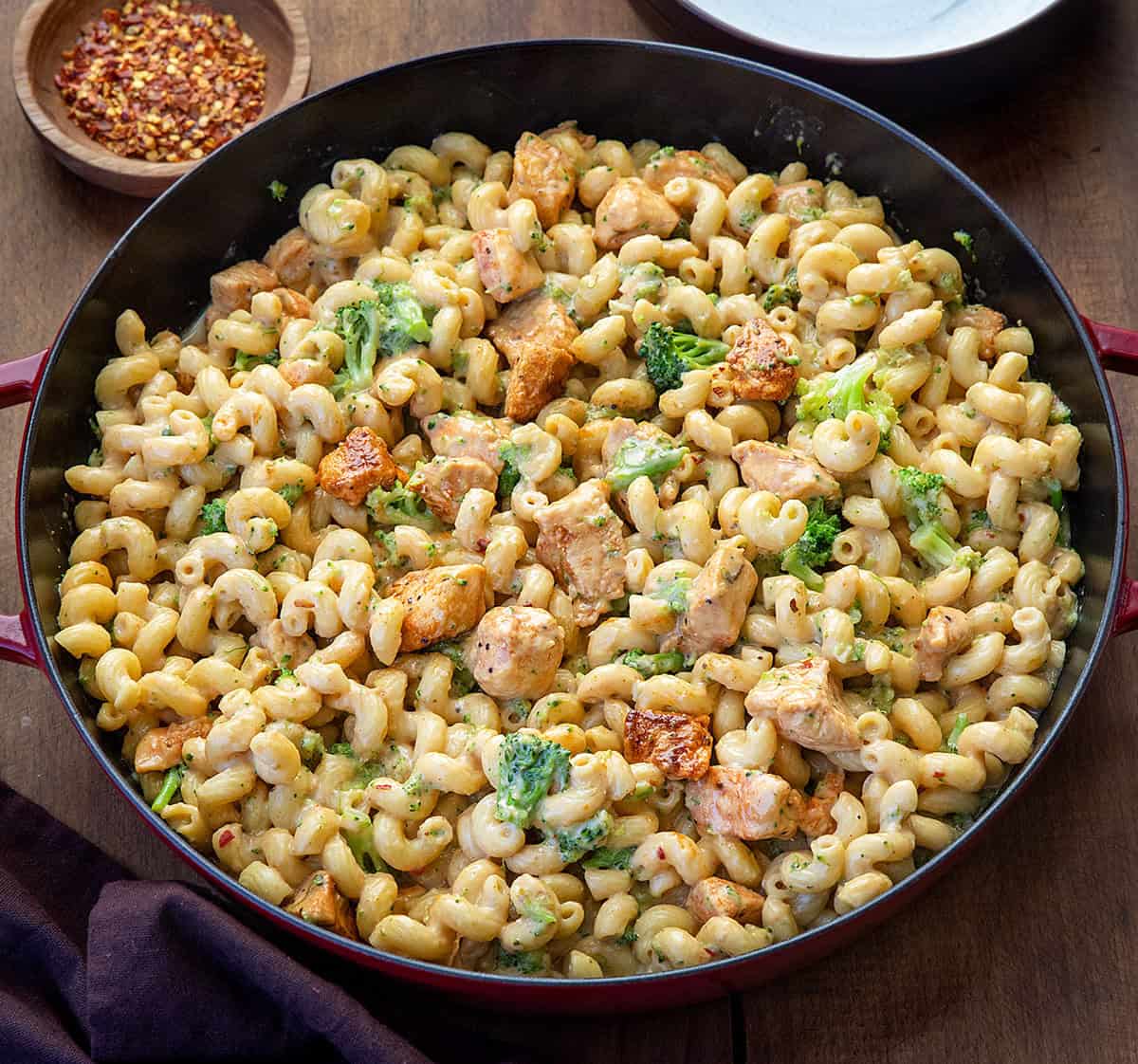 This White Cheddar Chicken Pasta with Broccoli is a creamy, comforting dinner made with tender chicken, cavatappi pasta, and crisp-tender broccoli all coated in a smooth white cheddar cheese sauce! View of a red skillet filled with White Cheddar Chicken Pasta with Broccoli.